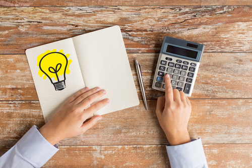 business idea, education, people and technology concept - close up of female hands with calculator, pen and lighting bulb drawing in notebook on table