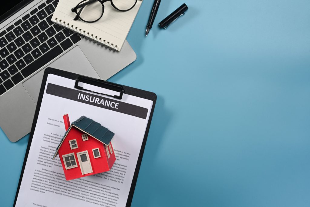 Top view laptop computer, house model ad notepad on blue background. Concept of real estate investors and leasing insurance