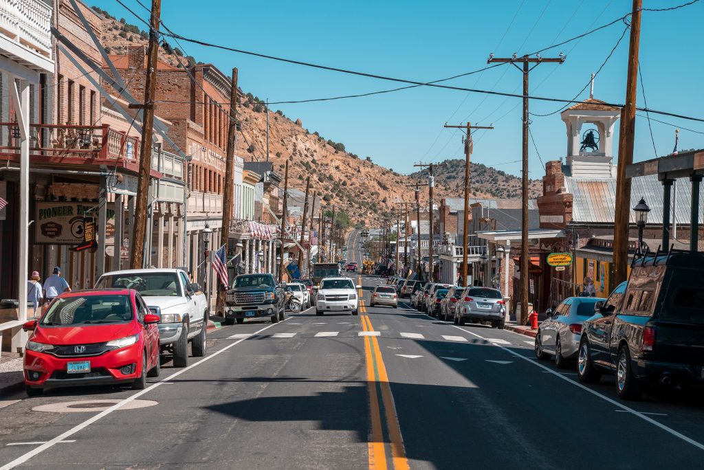 Cars on road amidst old shops at historic city with clear blue sky in background