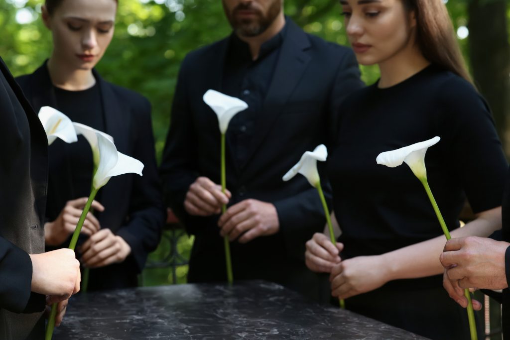 People with calla lily flowers near granite tombstone at cemetery