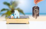 Miniature house on old book with house key in girl hand over blurred tropical beach background, property and real estate investment business, house insurance