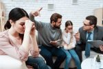 Upset woman sits in foreground and listens man with little girl communicates with psychotherapist.